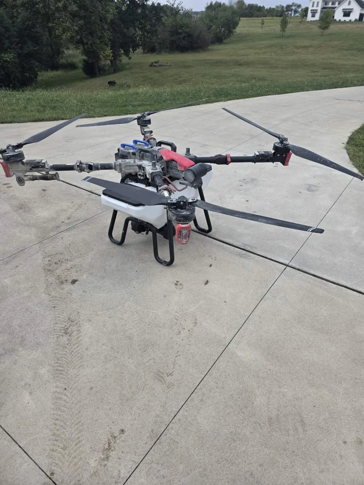 An agricultural spray drone with its rotor arms unfolded, sitting on a driveway ready to fly.