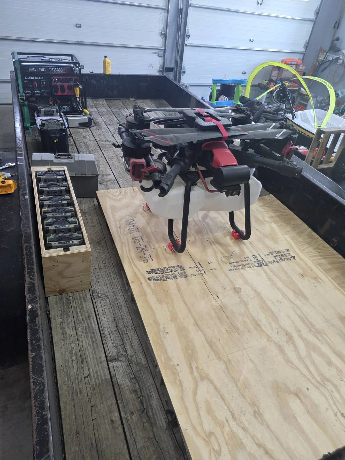 A spray drone loaded on a flatbed trailer beside a rack of charged flight batteries and a generator.